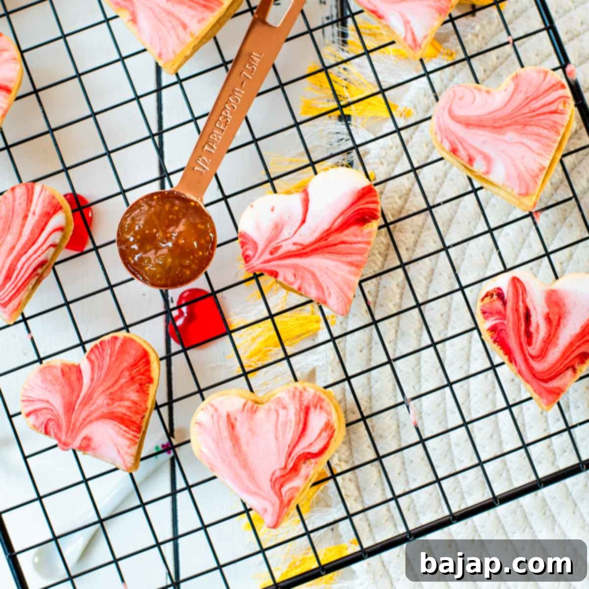 Gorgeous heart shaped sugar cookies with marbled icing, and filled with fig jam. Placed on cooling rack next to half a tablespoon of fig jam.