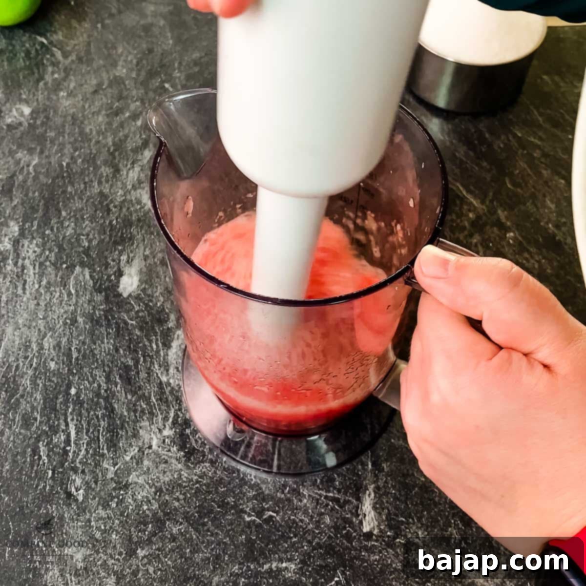 Blending watermelon pieces in a tall container using an immersion blender for a smooth puree.