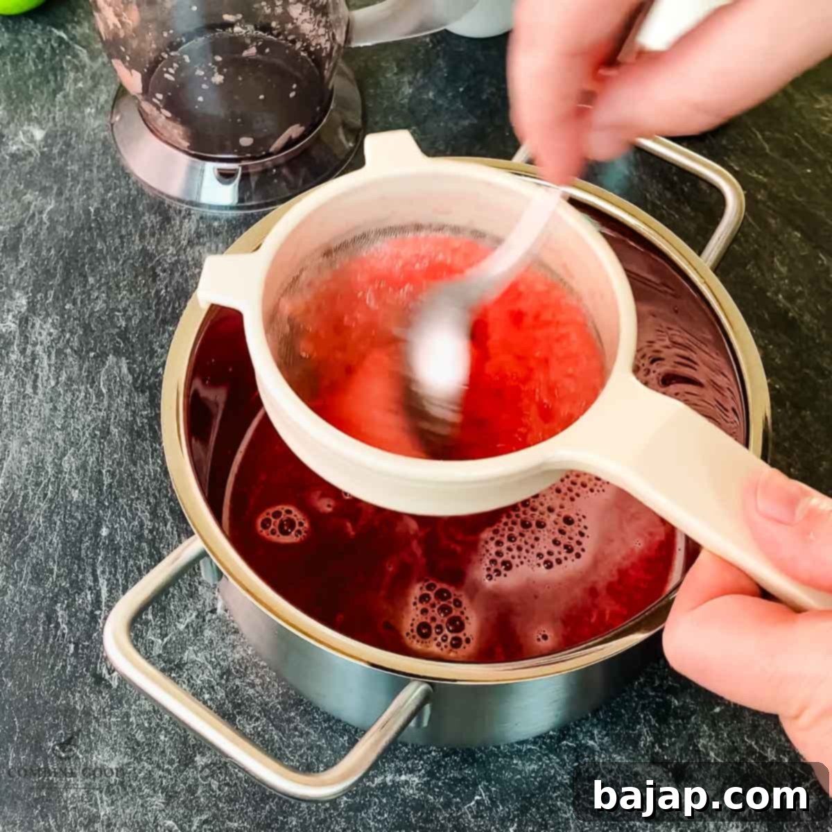 Using a spoon to press watermelon puree through a fine-mesh sieve, extracting all the juice.