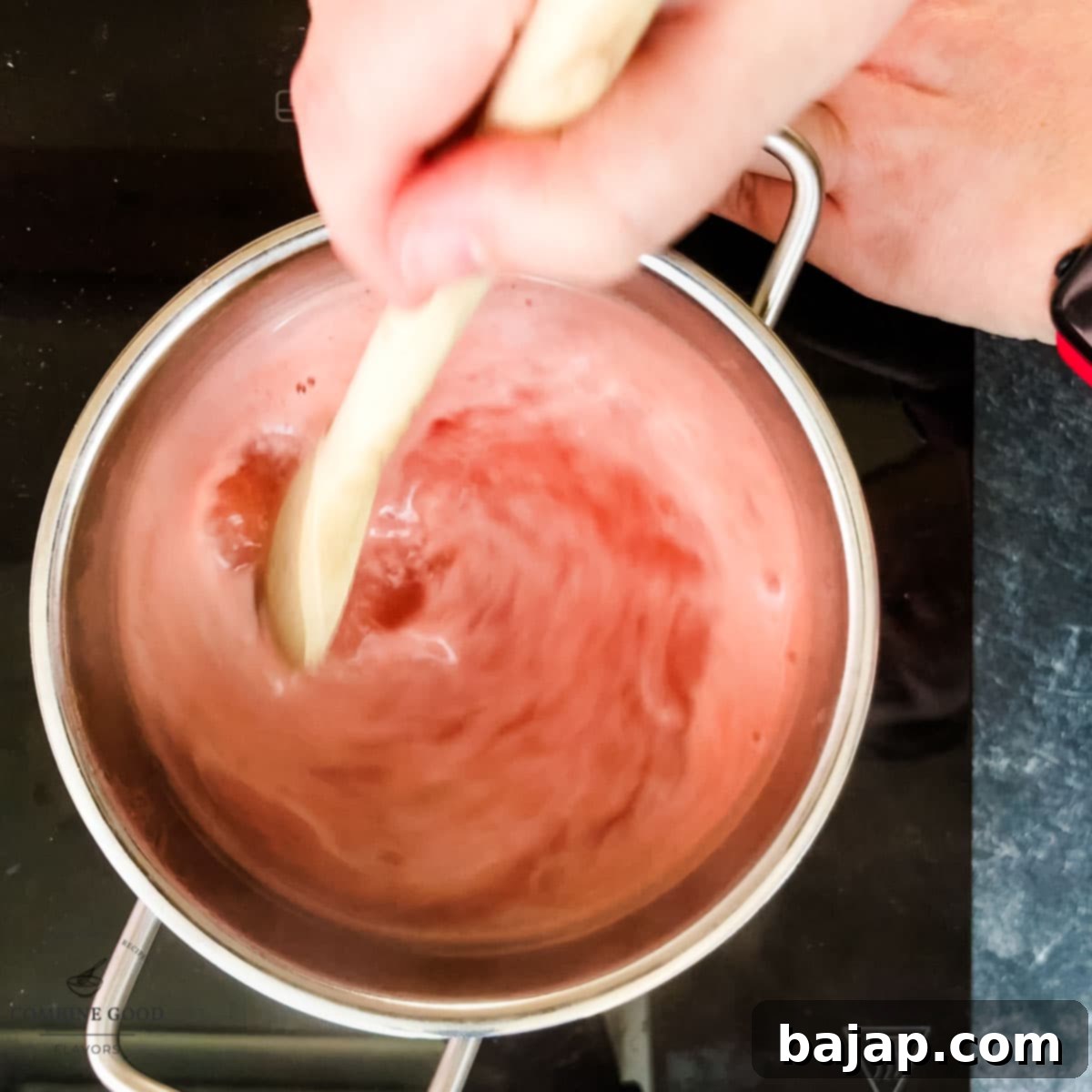 Watermelon syrup being stirred while simmering gently in a saucepan.