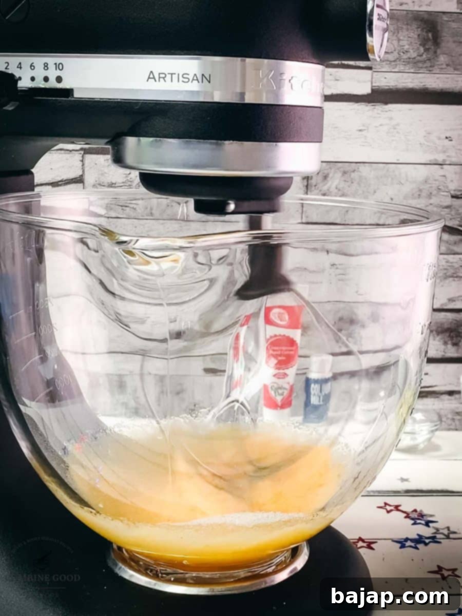 Kitchen machine with a whisk attachment, mixes yellow cake batter, prior to adding red food coloring.