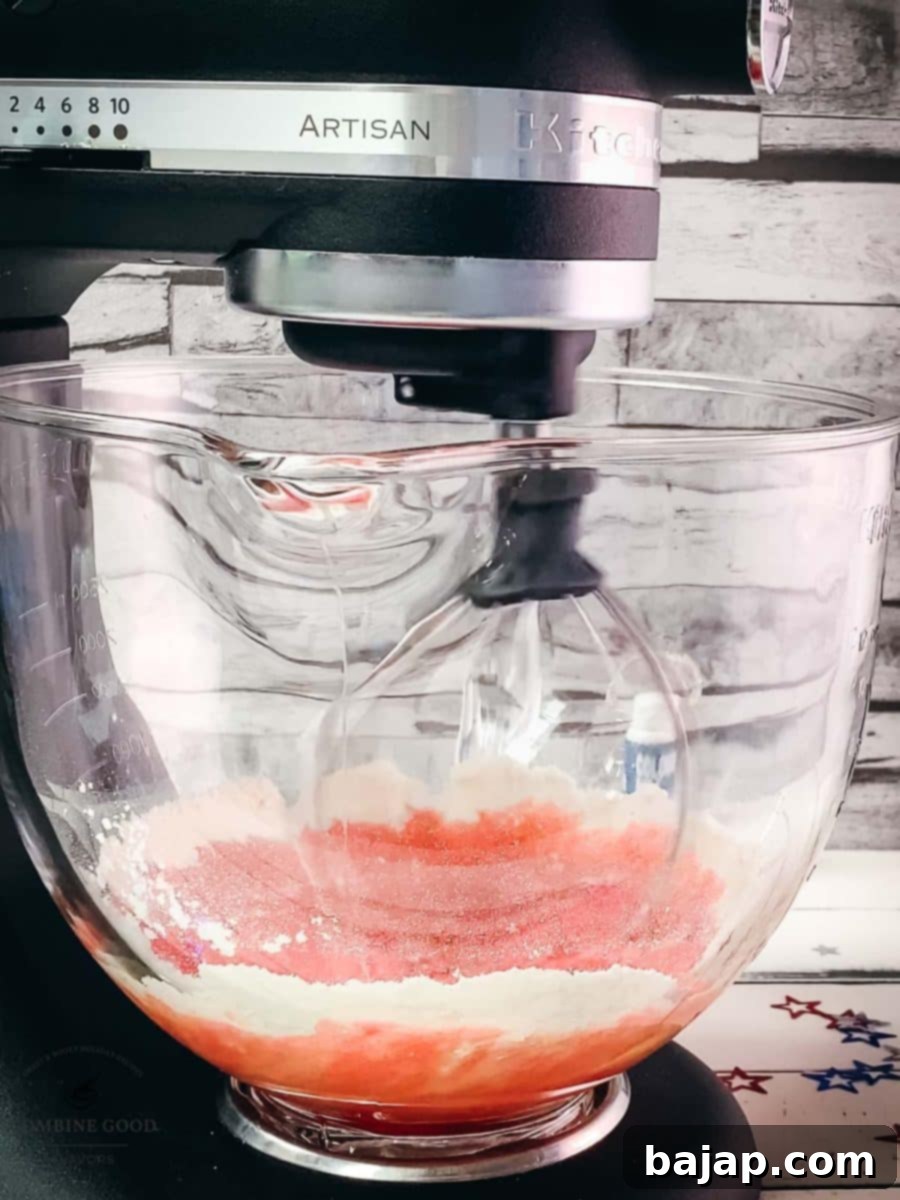 Kitchen machine with a whisk attachment, mixes vibrant red cake batter, ready for cupcake tins.