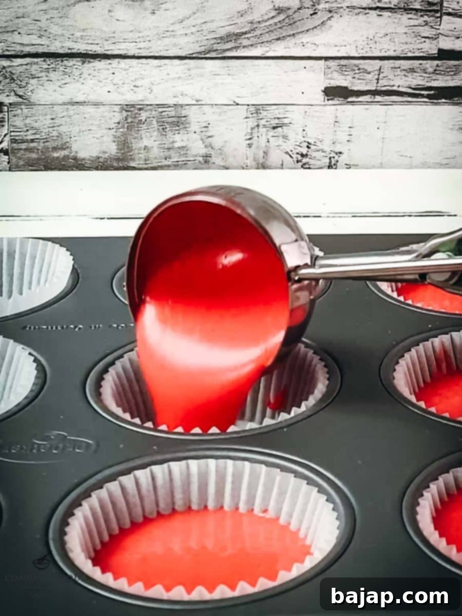 Ice cream scoop expertly pours red cake batter into the muffin tin, ensuring even distribution.