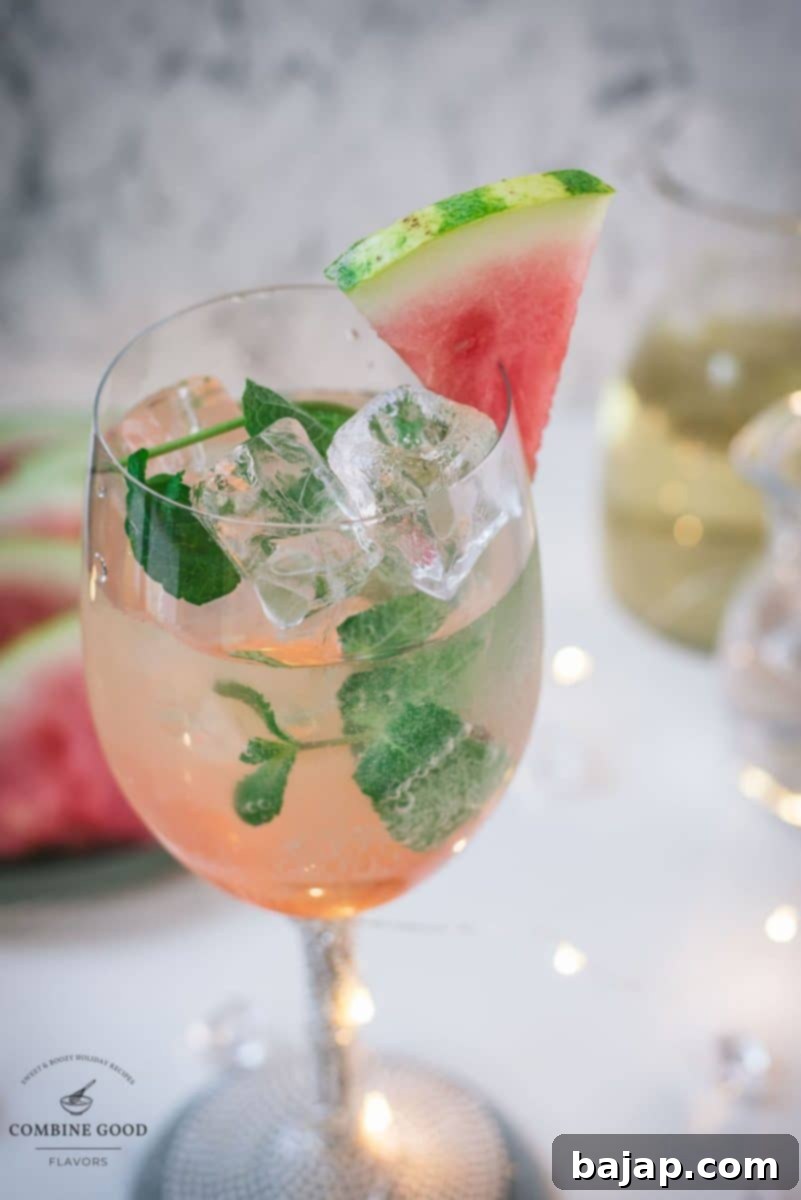 Gorgeous wine glass filled with watermelon spritzer, garnished with a watermelon slice and mint leaves.