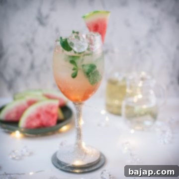 Gorgeous wine glass filled with watermelon spritzer, garnished with a watermelon slice and mint leaves.