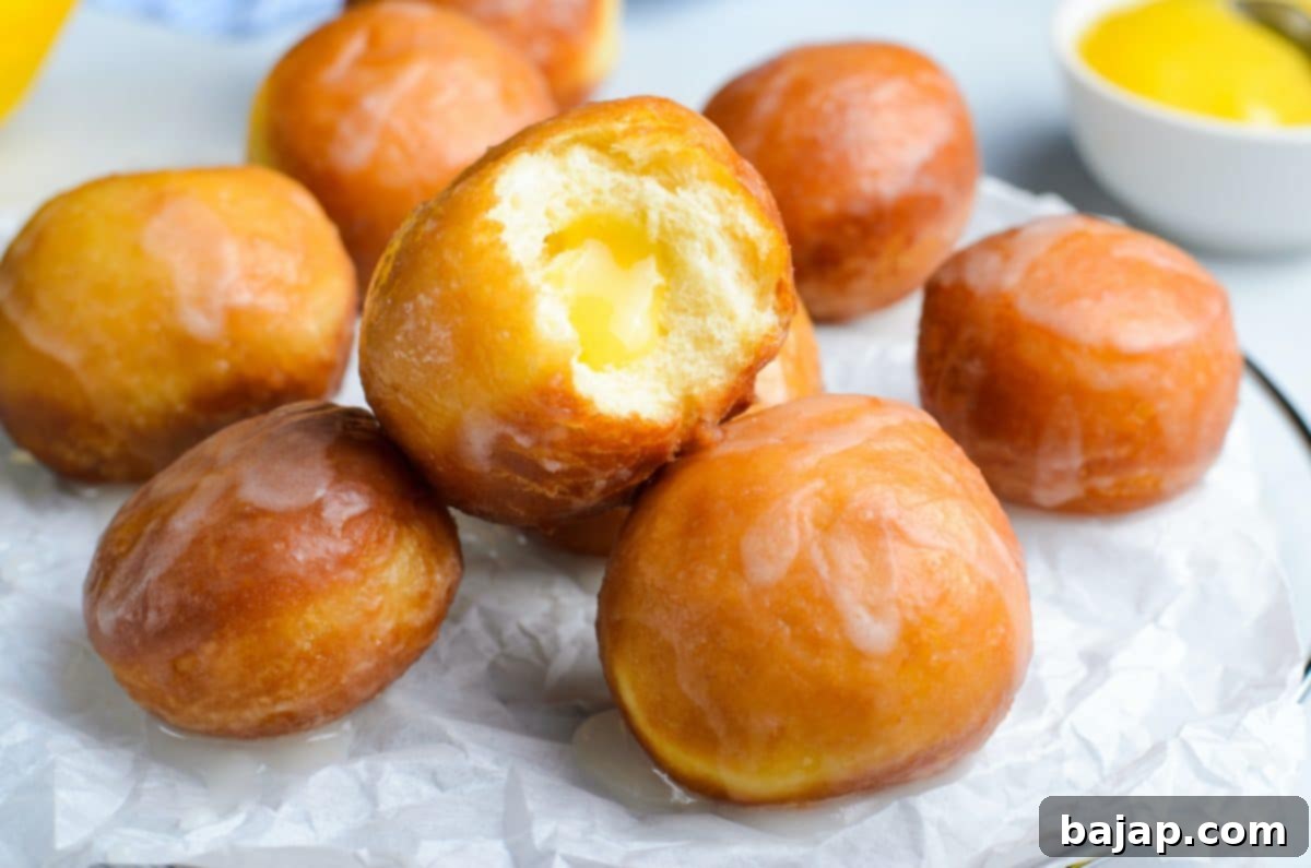 Glazed lemon curd donut holes piled on a white plate.