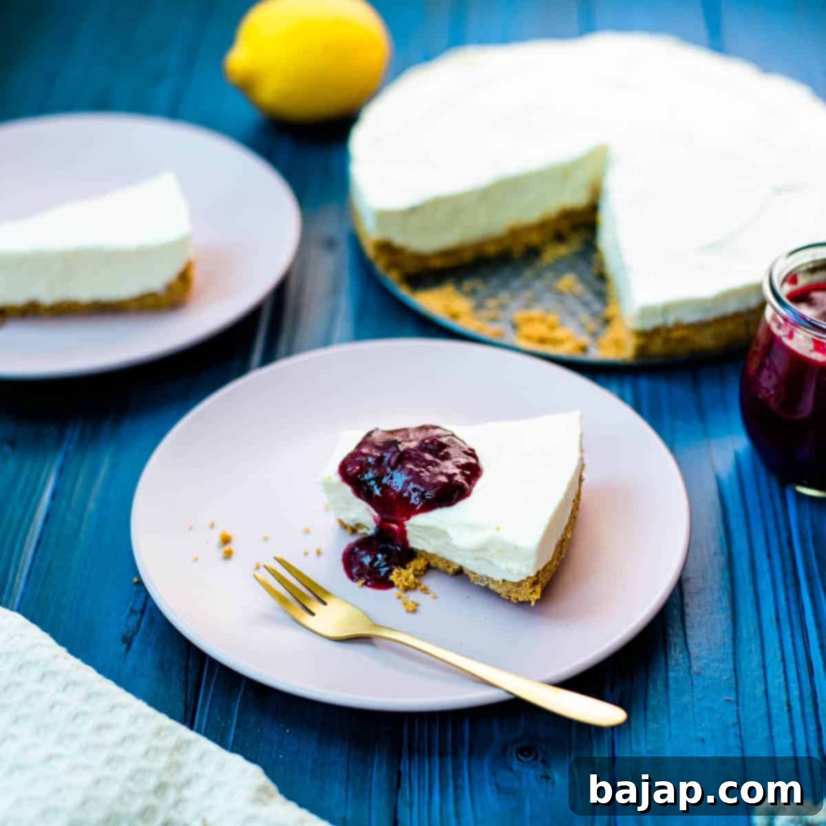 Refreshing lemon cheesecake slice with homemade blueberry sauce on dark blue wooden background.