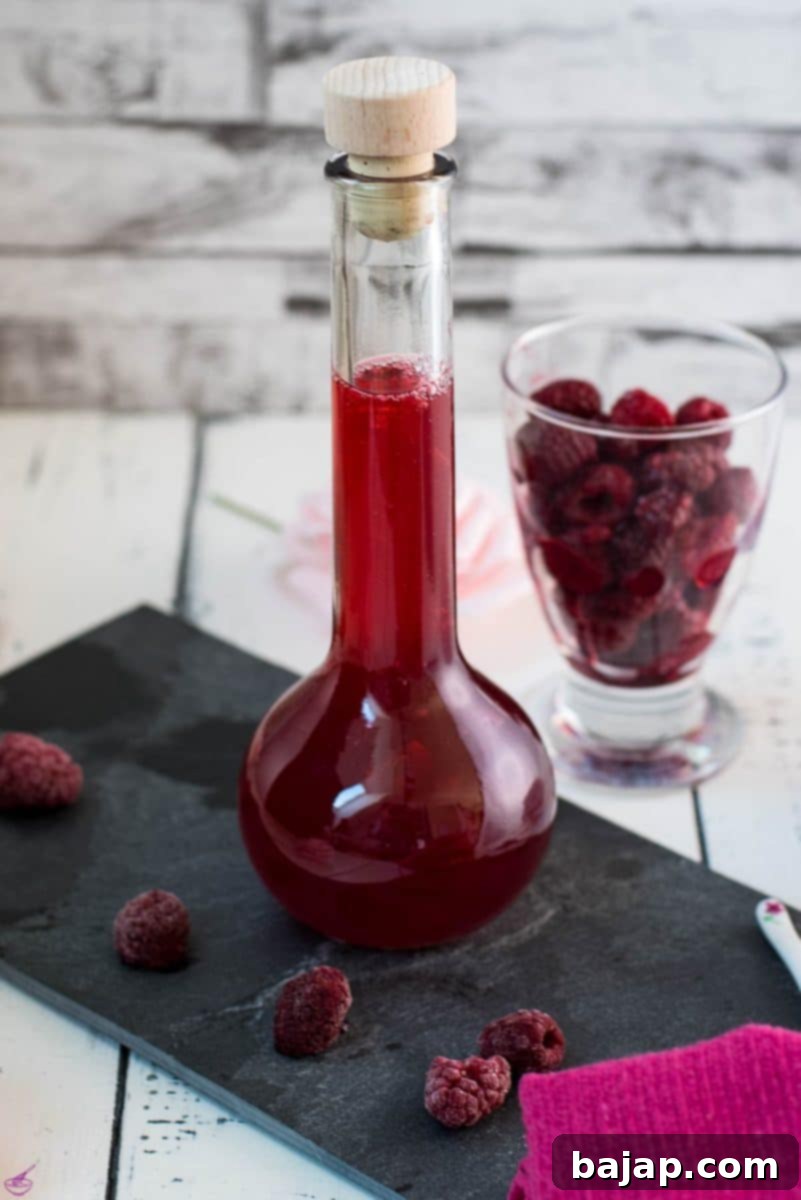 Flask filled with homemade raspberry syrup, placed on a black slate plate, ready to be used in cocktails.