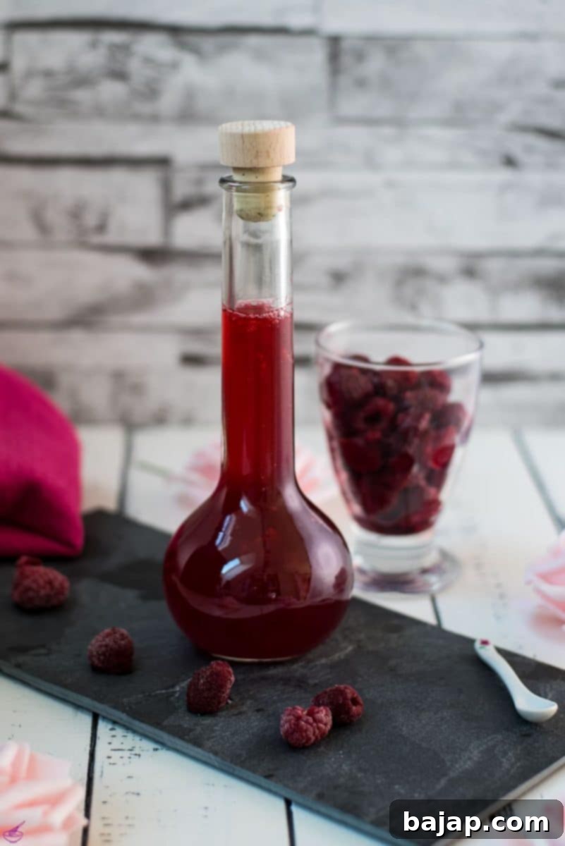 Flask filled with homemade raspberry syrup, placed on a black slate plate, ready to brighten any drink.