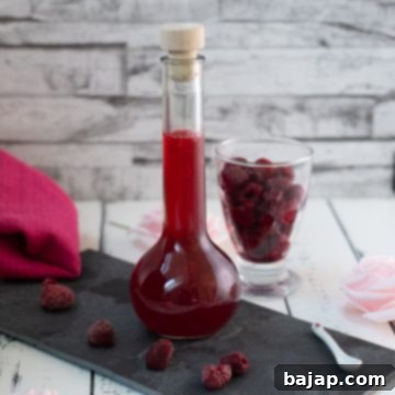 Flask filled with homemade raspberry syrup, placed on a black slate plate, vibrant and fresh.