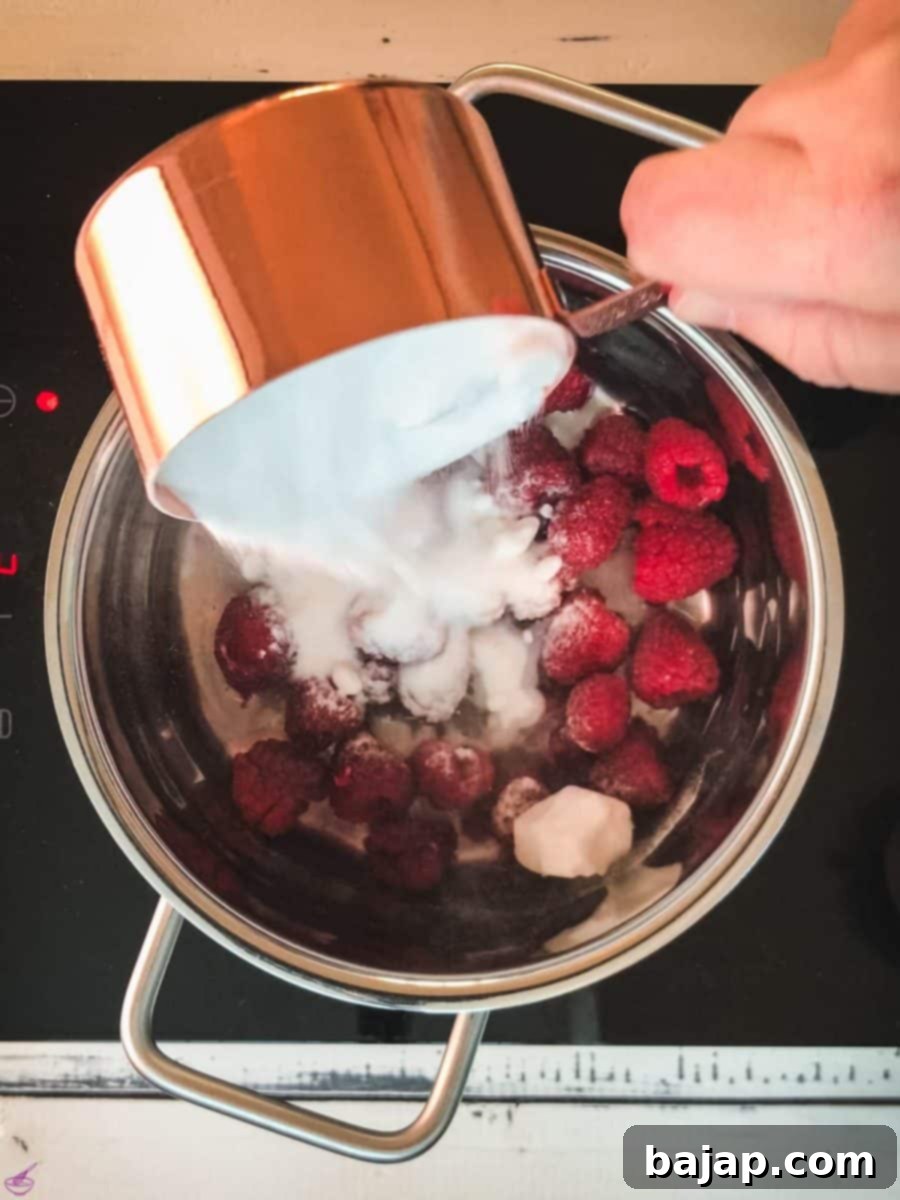 Pouring sugar into a saucepan filled with water and fresh raspberries for homemade syrup.