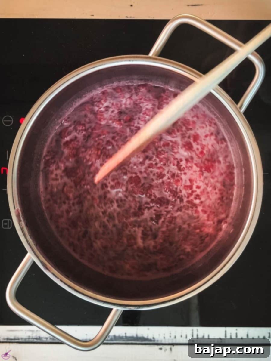 Saucepan filled with raspberry sauce with a wooden spoon across.