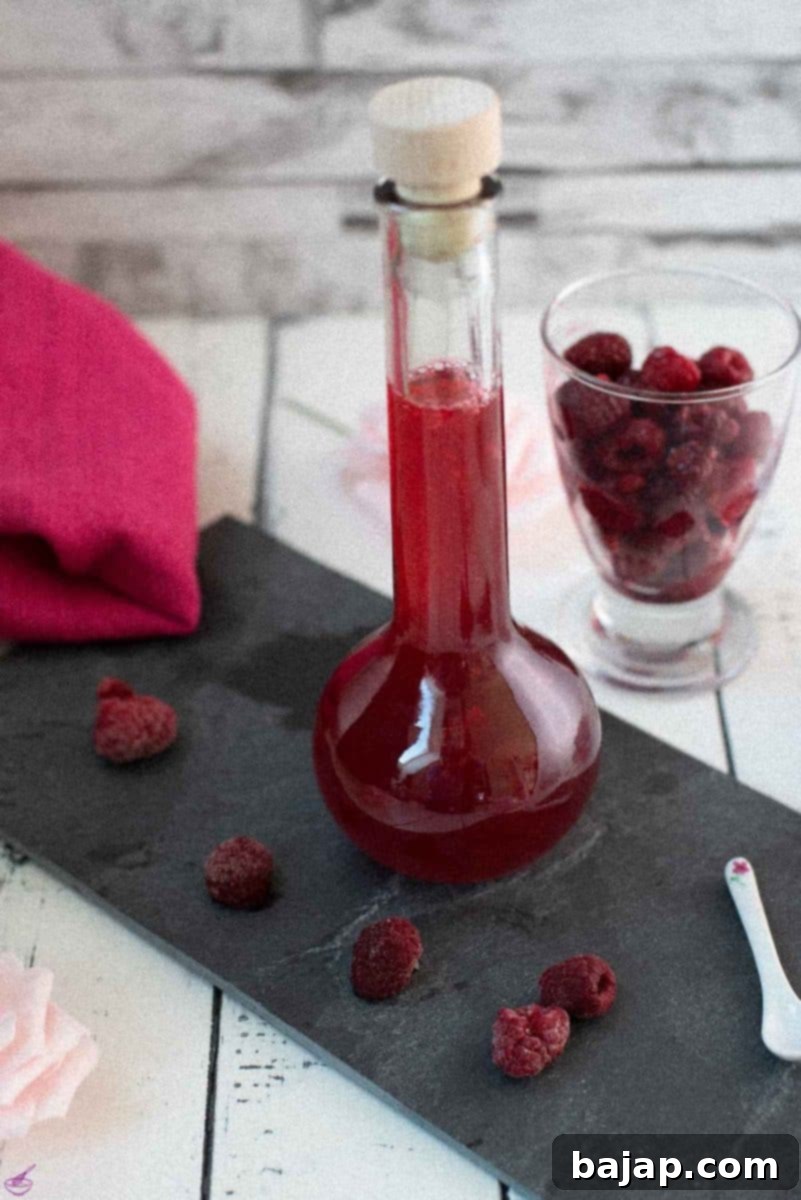 Flask filled with homemade raspberry syrup, placed on a black slate plate, showcasing the rich color.