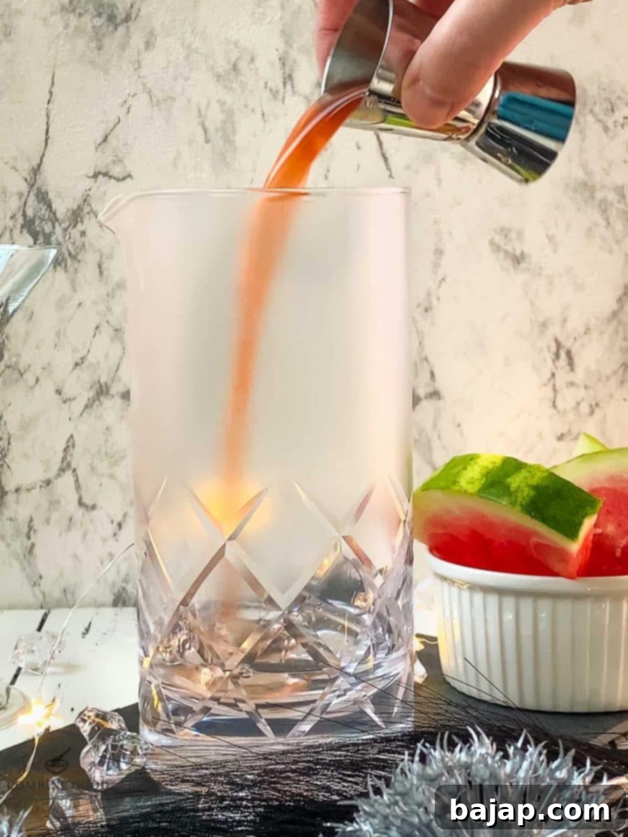 Adding homemade watermelon syrup into the stirring glass, creating a beautiful rosy hue.