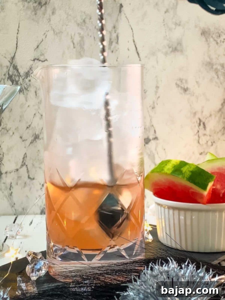 Barspoon stirring the watermelon martini in a stirring glass, ensuring perfect chilling.