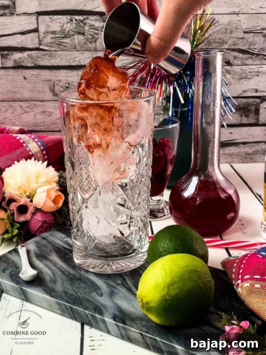 Pouring sloe gin over cubed ice into a highball glass.
