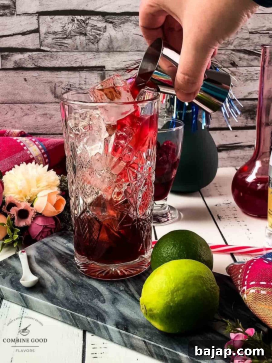 Pouring sweet raspberry syrup over the cubed ice into a highball glass.