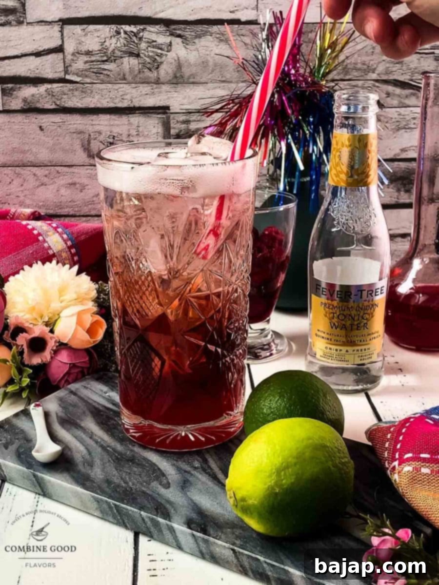 Placing a stylish red and white drinking straw and a lime wedge into the finished raspberry gin and tonic cocktail.