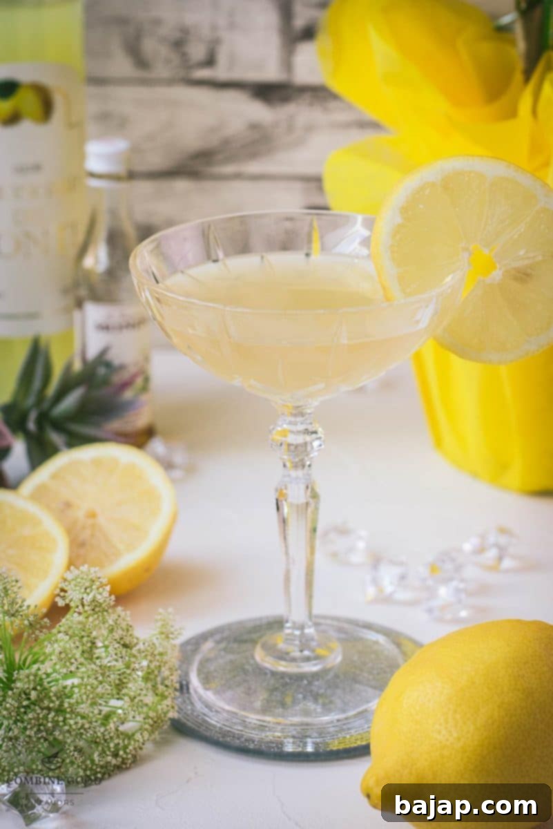 A beautifully crafted Limoncello Martini with elderflower syrup, garnished with a fresh lemon slice, resting on a sophisticated mirrored coaster. The cocktail is a vibrant yellow, inviting and refreshing.