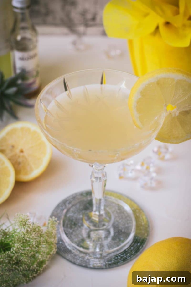 A stunning Limoncello Martini with elderflower syrup, garnished with a vibrant lemon slice, presented on a chic mirrored coaster. The cocktail glows with a refreshing yellow hue.