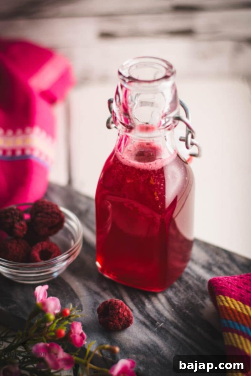 Preserving bottle, filled with delicious uncooked raspberry syrup placed on a marbled plate.
