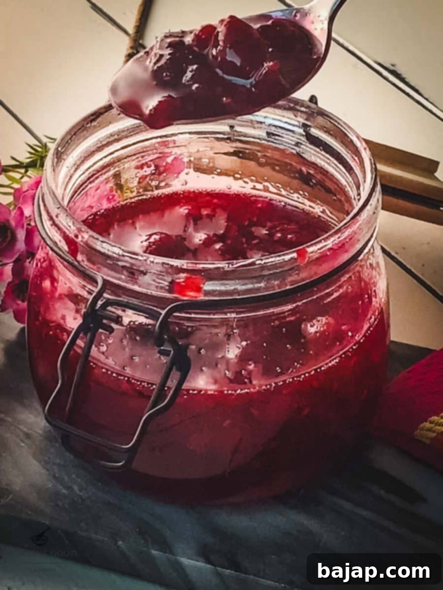 Spoon with raspberry sauce hovering over a preserving jar filled with raspberry sauce.