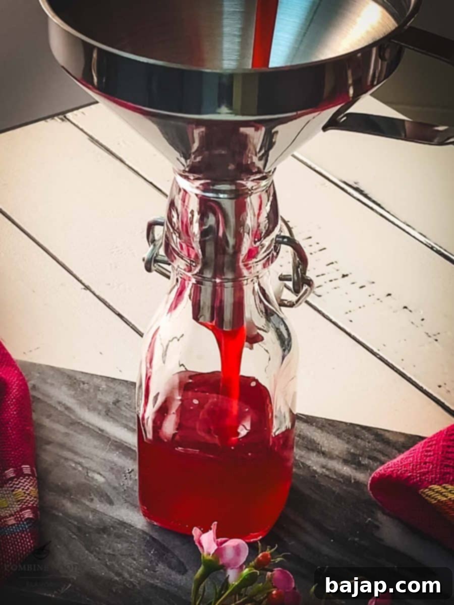Pouring the finished raspberry syrup into a preserving bottle using a funnel.