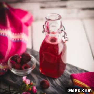Preserving bottle, filled with delicious uncooked raspberry syrup placed on a marbled plate.