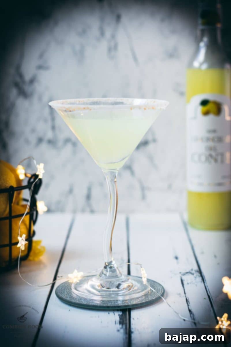 Gorgeous Limoncello vodka martini with orange sugar rim, placed on a mirrored coaster on a white wooden board.