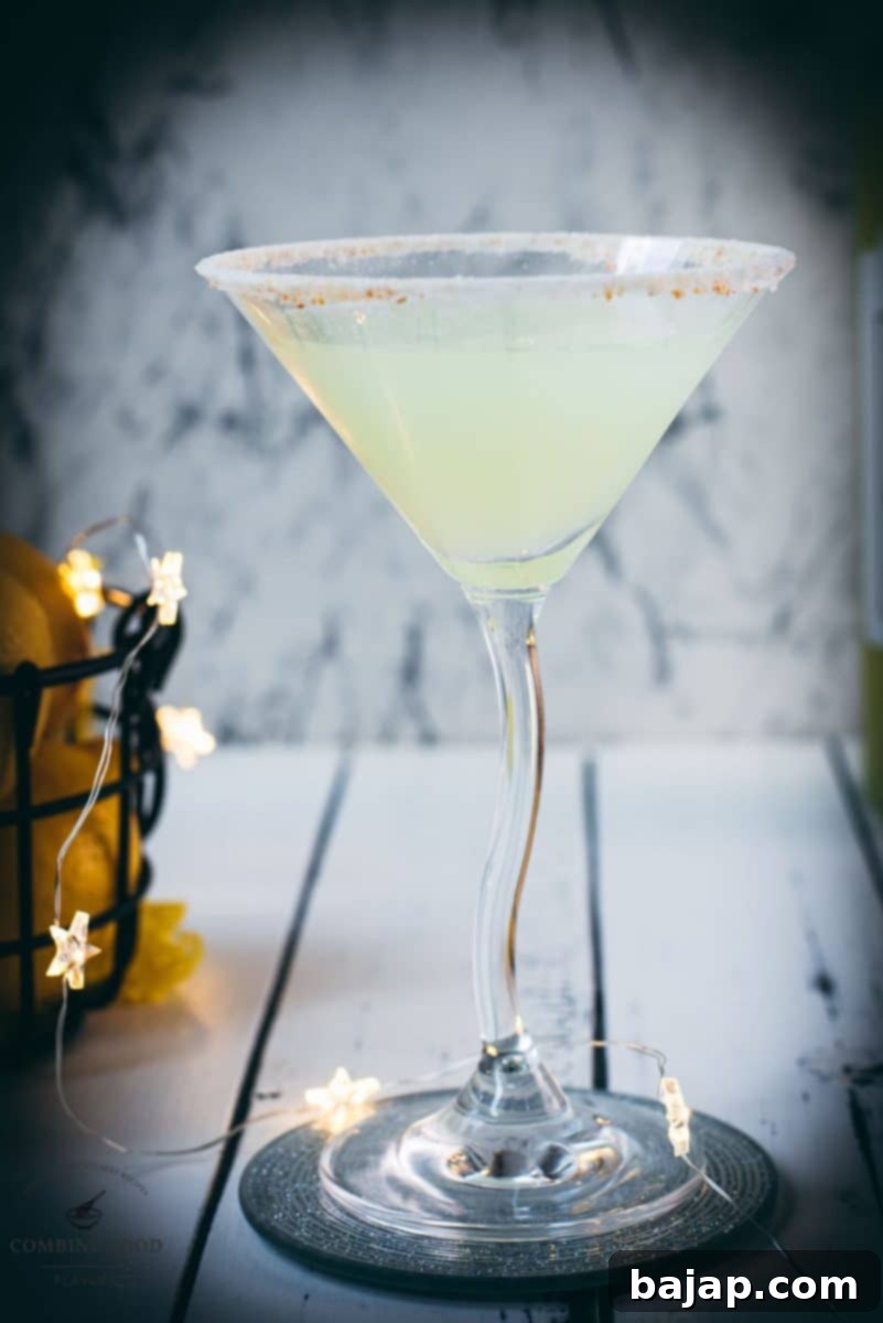 Gorgeous Limoncello vodka martini with orange sugar rim, placed on a mirrored coaster on a white wooden board.