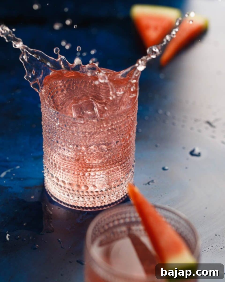 A glass of easy watermelon vodka cocktail, garnished with a watermelon wedge and a sprig of mint.