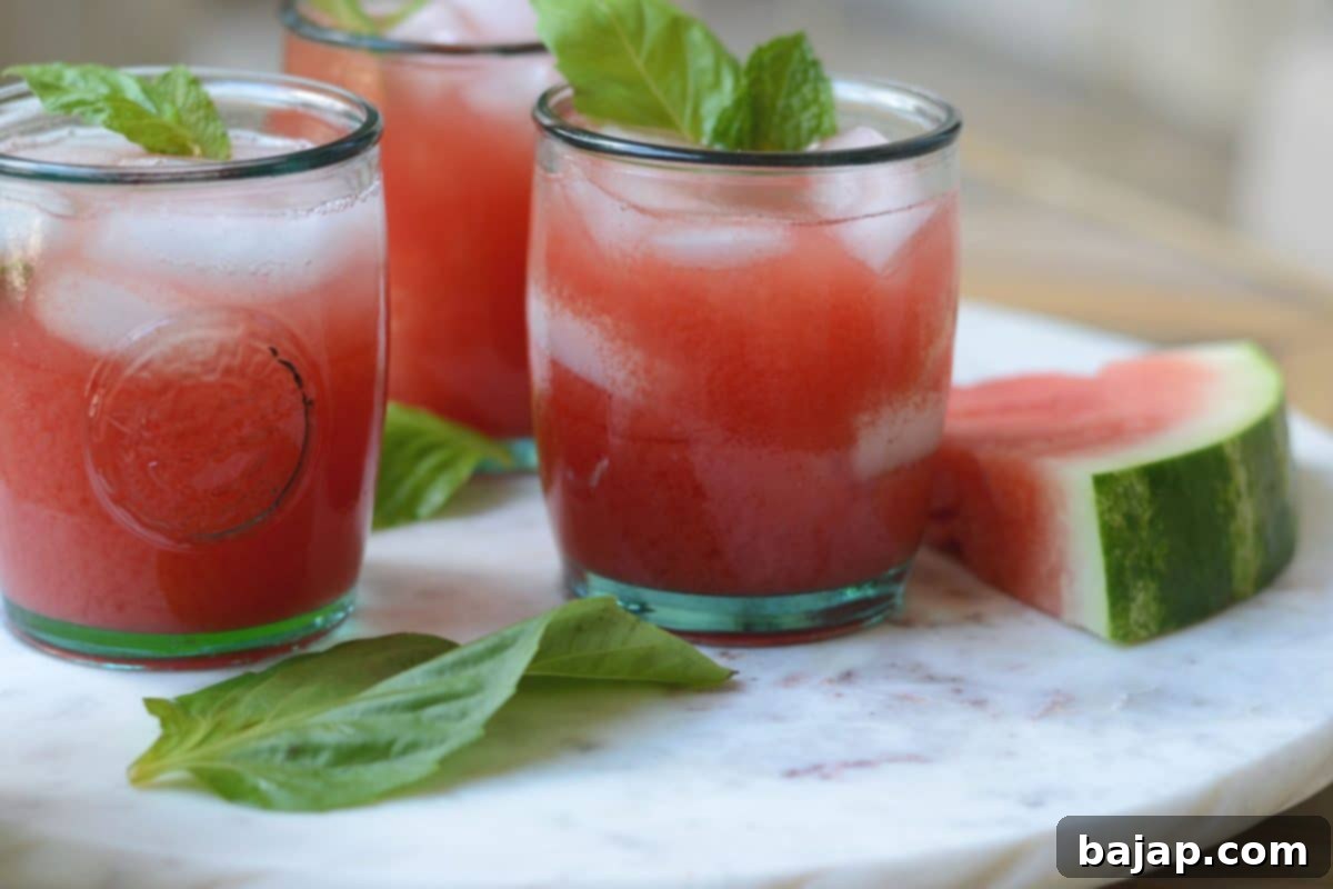 Two glasses of vibrant watermelon cocktails with rum, basil, and mint, garnished with fresh herbs.