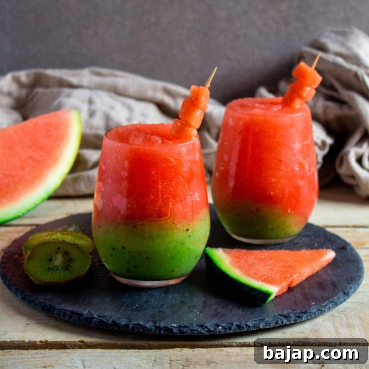 A vibrant green and red kiwi watermelon slushie in a glass, with fresh kiwi slices.