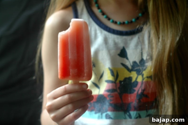 Homemade pineapple watermelon popsicles, layered with yellow and red fruit, on a wooden board.