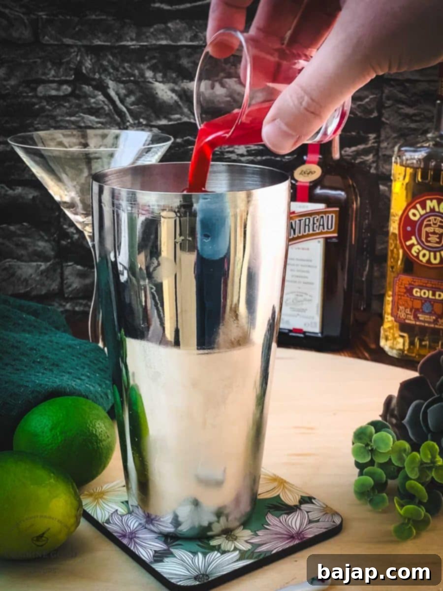 Pouring rich, homemade raspberry syrup into the cocktail shaker.