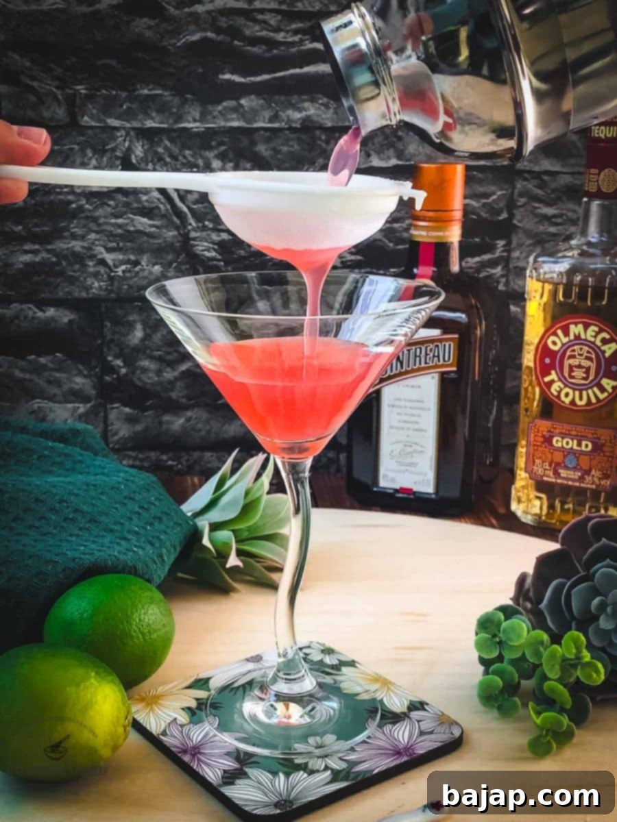 A cocktail being fine-strained from a shaker into a sleek cocktail glass, ensuring a smooth texture.