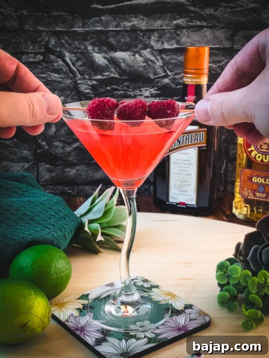 Garnishing the finished raspberry margarita with fresh raspberries on a decorative cocktail spike.