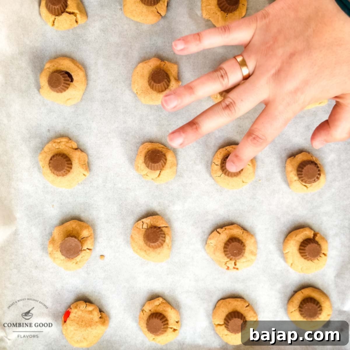 Placing one peanut butter cup on top of each baked peanut butter cookie.