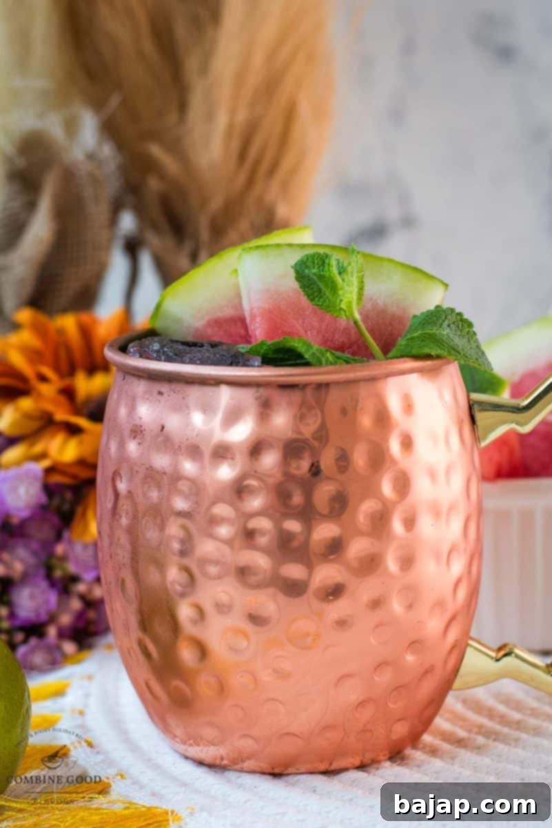 A gorgeous copper mug, brimming with a perfectly mixed Watermelon Moscow Mule, artfully garnished with fresh watermelon slices and fragrant mint leaves, ready to be enjoyed on a warm day.