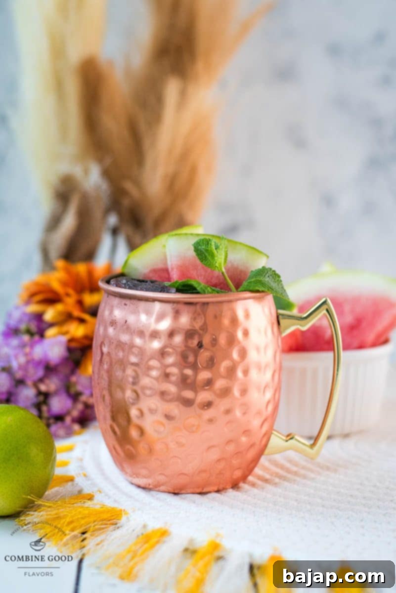 A stunning Watermelon Moscow Mule cocktail, perfectly mixed and garnished, sits in a gleaming copper mug, highlighting the drink's vibrant colors and refreshing appeal.