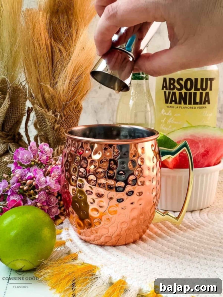 Pouring homemade watermelon syrup into a shiny copper mug, the first step to a delicious Watermelon Moscow Mule.