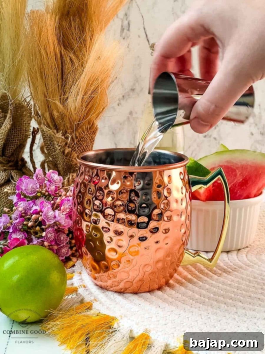 Adding smooth vanilla vodka into a copper mug already containing watermelon syrup, preparing for the next step of the Moscow Mule.