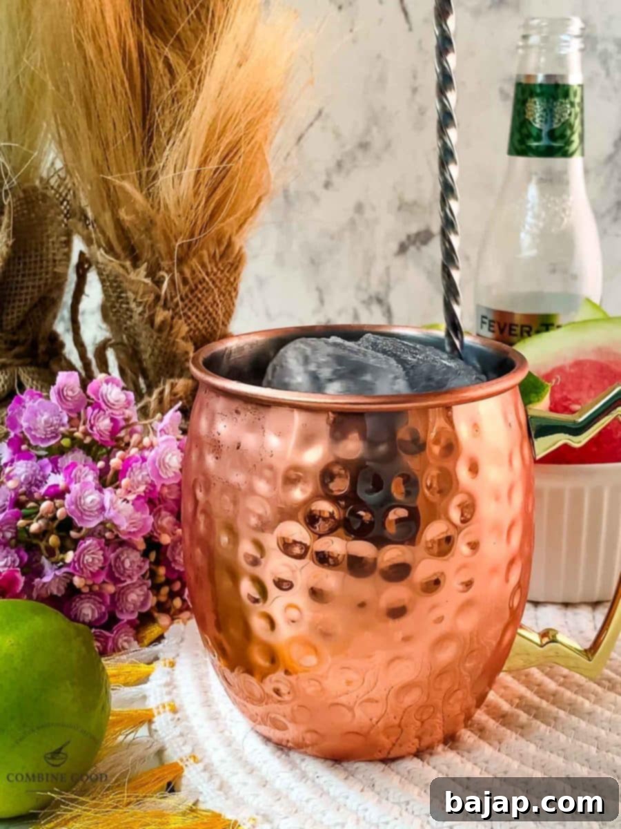 A bar spoon gently stirring the Watermelon Moscow Mule in a copper mug, mixing the ingredients without losing the fizz.