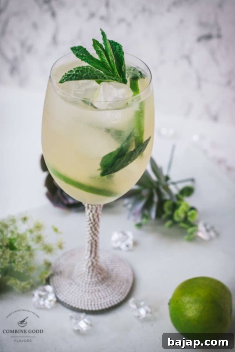 Stunning wine glass filled with Hugo spritz cocktail, placed on a white plate and garnished with mint leaves and lime slices.