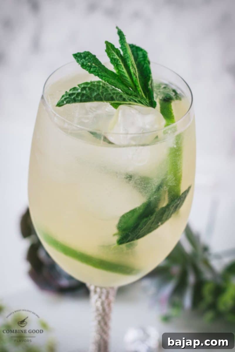 Stunning wine glass filled with Hugo spritz cocktail, placed on a white plate and garnished with mint leaves and lime slices.