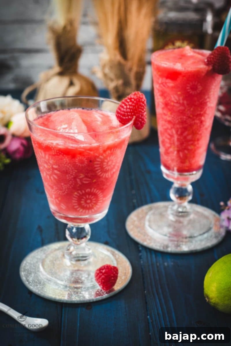 Raspberry Chill Margarita 2 Two vibrant pink frozen raspberry margaritas, perfectly blended and garnished with fresh raspberries, sitting on stylish glass coasters, ready to be enjoyed.