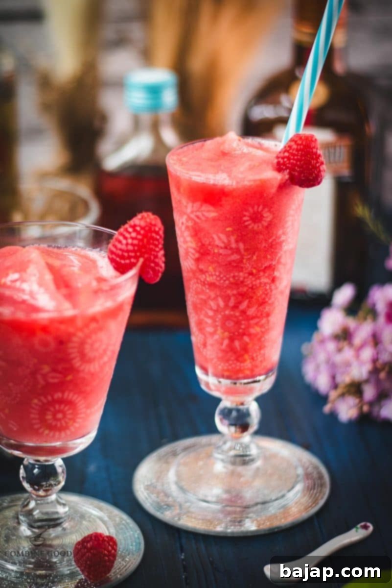 Two gorgeous glasses filled with a delicious frozen raspberry margarita cocktail, placed on glass coaster.