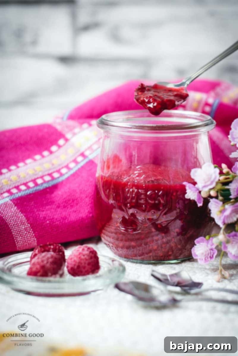 Vibrant raspberry cheesecake topping in a preserving jar, placed on white structured ground.