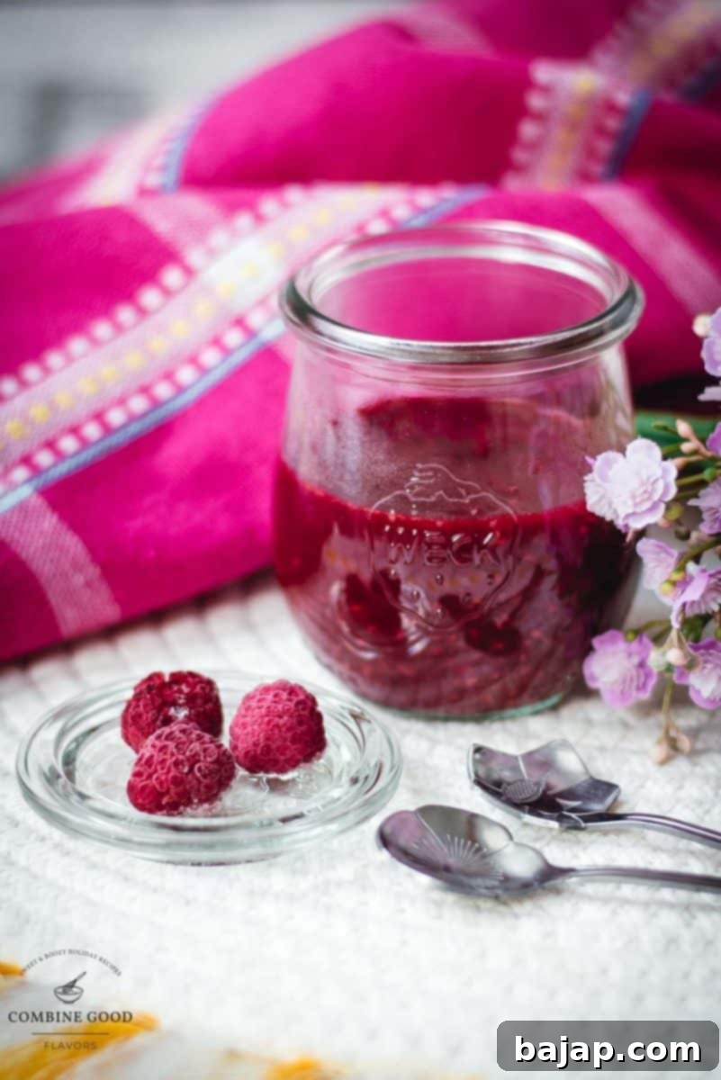 Vibrant raspberry cheesecake topping in a preserving jar, placed on white structured ground.
