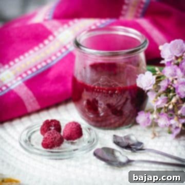 Vibrant raspberry cheesecake topping in a preserving jar, placed on white structured ground.